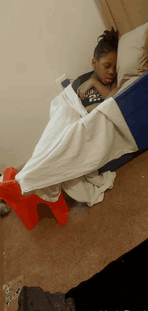 a child is sleeping in a bed with a blanket and a pillow on top of a blue crate