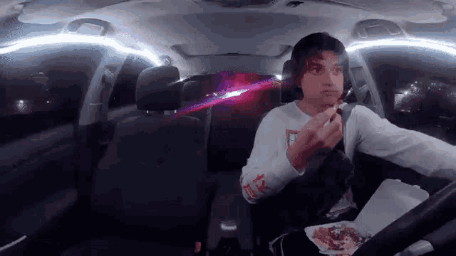 a man is driving a car and eating a pizza .
