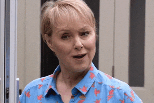 a woman in a blue shirt is standing in front of a door making a funny face .