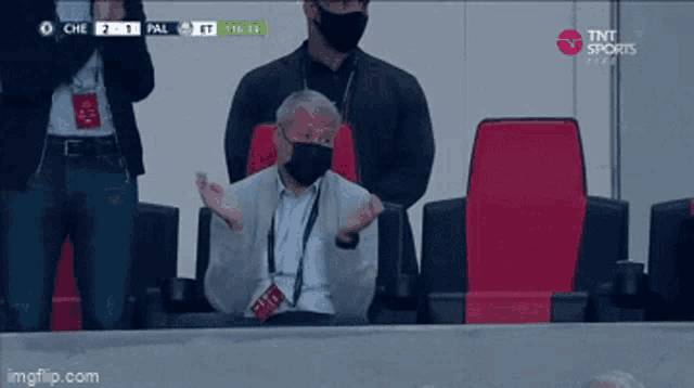 a man wearing a mask sits in a stadium watching a soccer game on tnt sports