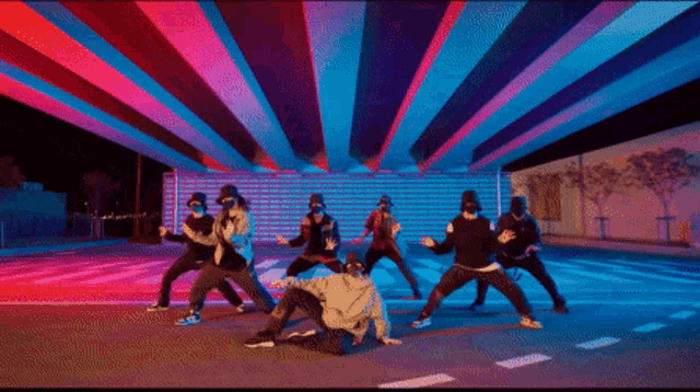 a group of men are dancing on a street with purple and blue lights behind them