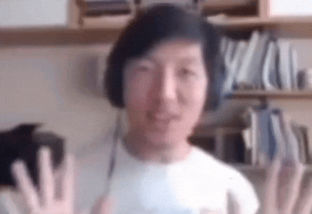 a man wearing headphones is giving a high five while sitting in front of a bookshelf .