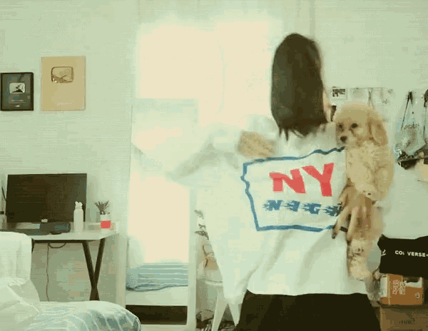a woman wearing a white ny sweatshirt is holding a small brown dog