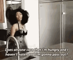 a woman in a black bra is standing in a kitchen next to a sink and refrigerator .