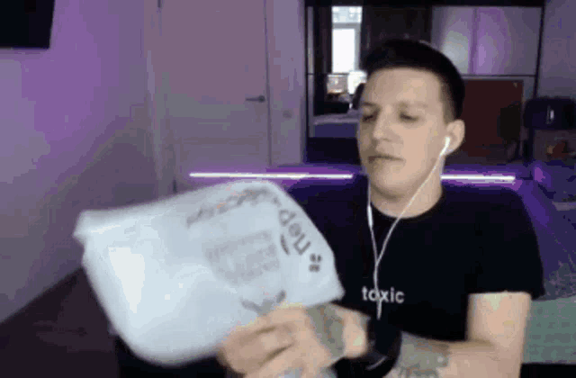 a man wearing headphones and a toxic shirt is holding a piece of paper in his hands .
