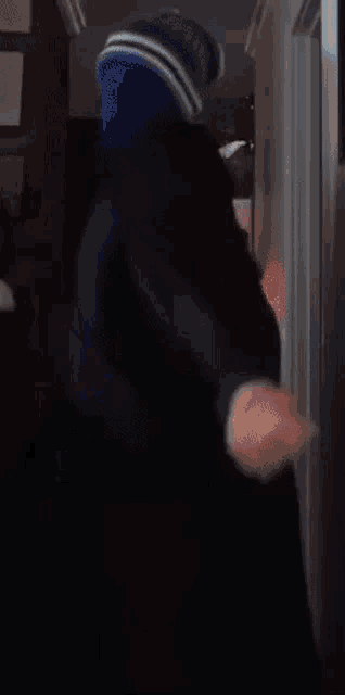 a person wearing a black jacket and a blue hat is standing in front of a refrigerator