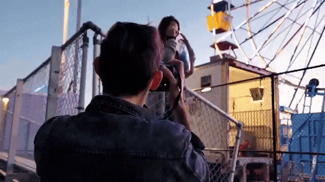 a man is taking a picture of a woman in front of a ferris wheel at a carnival