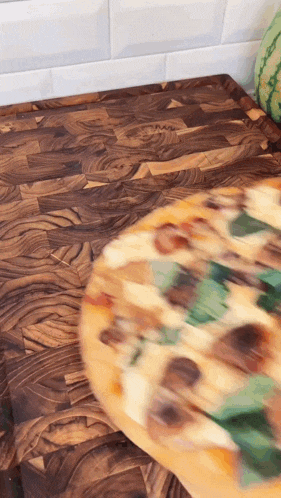 a pizza is being tossed on a wooden cutting board with a watermelon in the background