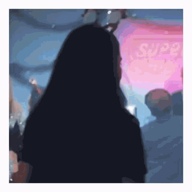 a woman with long black hair is standing in front of a stage in a club .