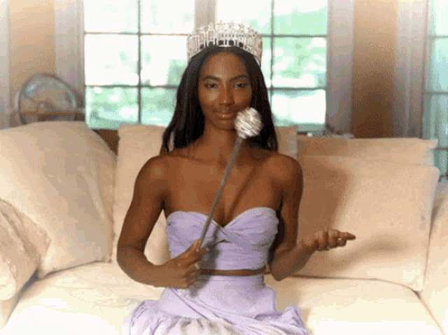 a woman with a tiara on her head holds a flower