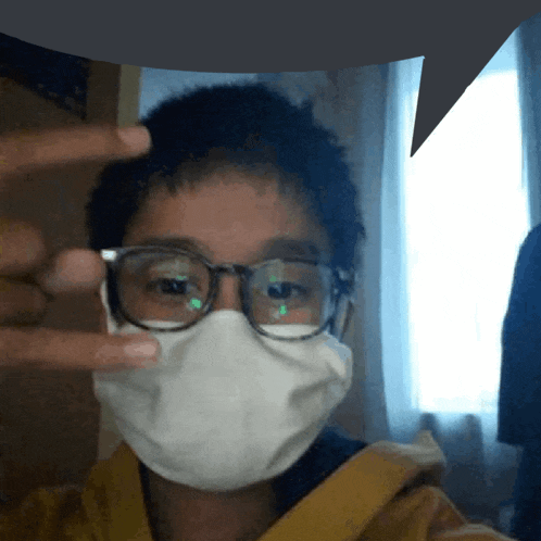 a young boy wearing glasses and a face mask makes a peace sign