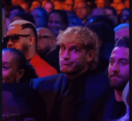 a man is making a funny face while sitting in a crowd .