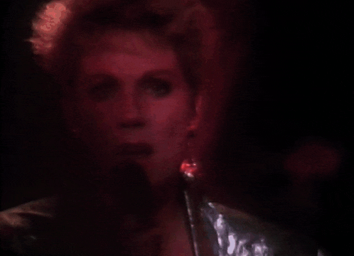 a woman singing into a microphone with red lights behind her