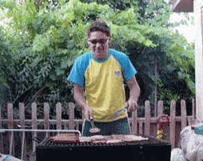 a man in a yellow and blue shirt is grilling meat