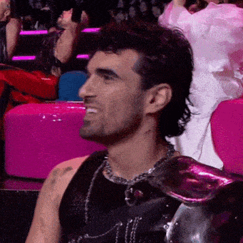 a man in a black tank top is sitting in a pink chair and smiling .