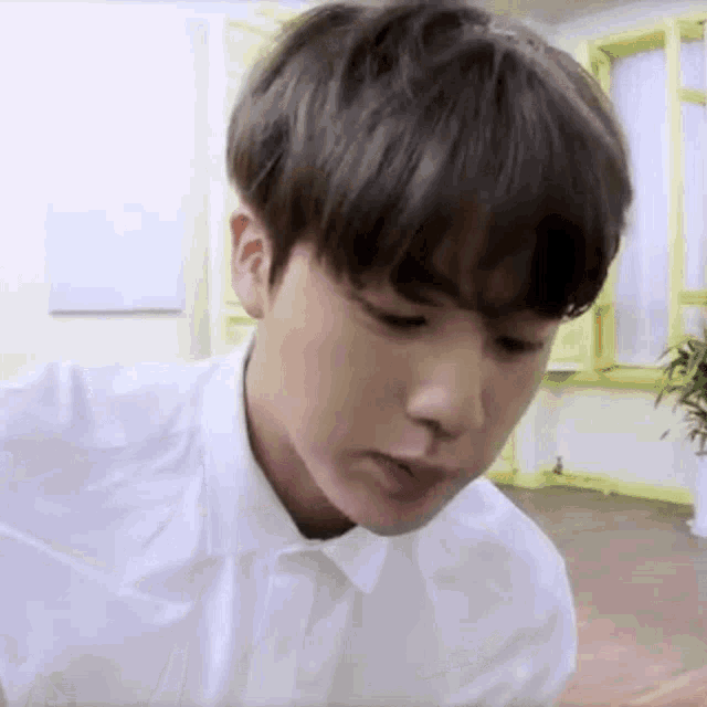 a young man in a white shirt is sitting in a room with a plant .