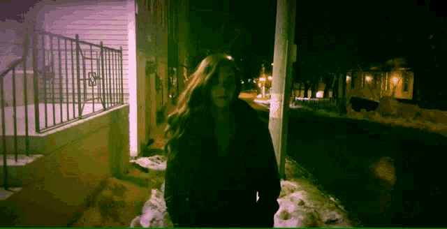 a woman in a black coat is walking down a snowy sidewalk at night