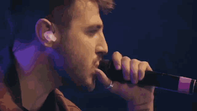 a man is singing into a microphone with a purple background