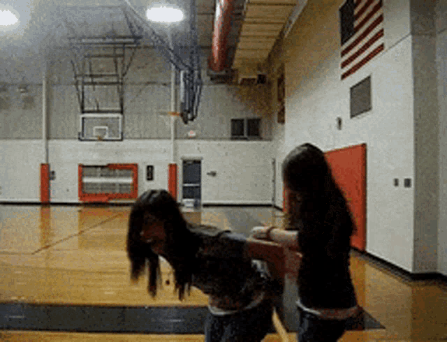 two girls are playing basketball in a gym with an american flag on the wall