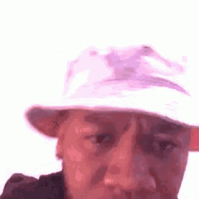a close up of a person wearing a bucket hat and looking at the camera .