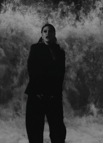 a black and white photo of a woman standing in front of a wall of smoke