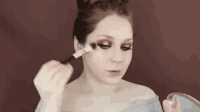 a woman is applying makeup on her face with a brush .