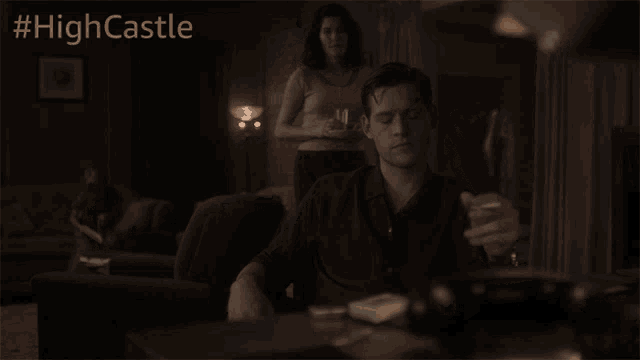a man sits at a table with a woman standing behind him and the hashtag #highcastle is above him