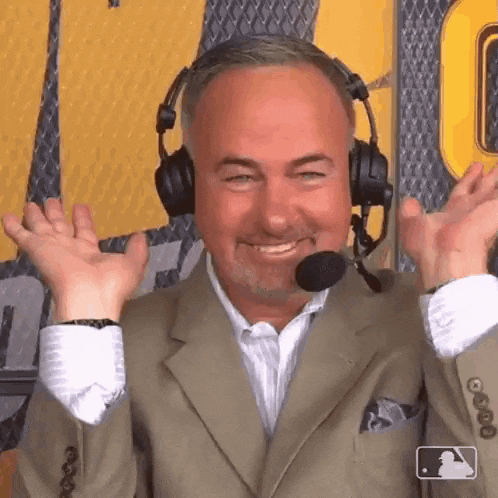 a man wearing headphones and a microphone is smiling with his arms outstretched .