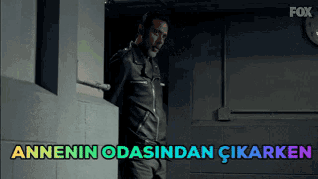 a man in a leather jacket is standing in a dark room with the words annenin odasindan çikarken above him