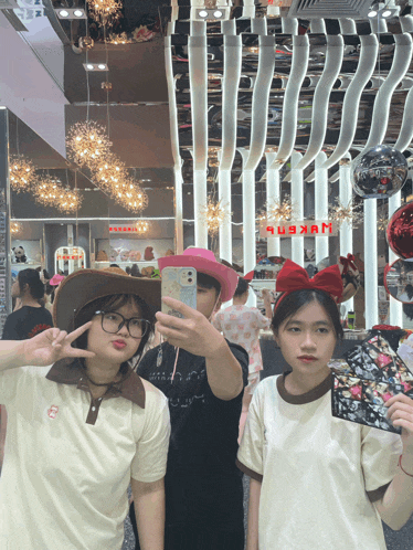three girls are taking a selfie in front of a sign that says ' nxkpb '