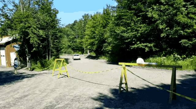 a white car is driving down a dirt road behind a yellow fence