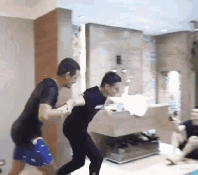 two men are fighting in a bathroom while a woman sits on a bed .