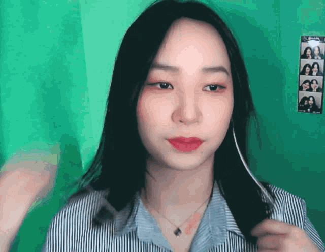 a woman in a striped shirt is holding her hair in front of a green wall