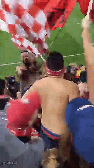a man without a shirt is standing in front of a soccer field with a celoerf watermark