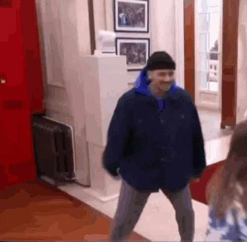 a man in a blue jacket and black hat is standing in a room