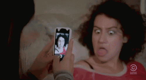 a woman is making a funny face while taking a picture of herself with a cell phone .