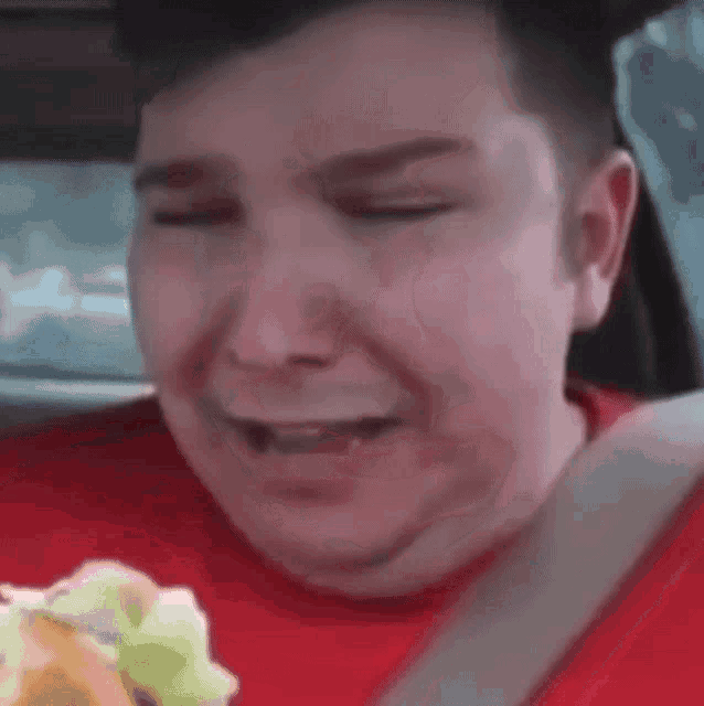 a man is eating a taco in a car with his eyes closed .