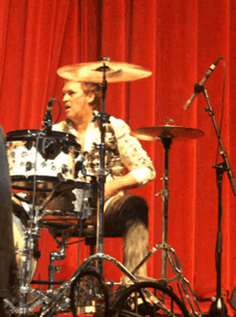 a man playing a drum set in front of a red curtain