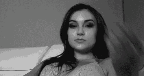 a black and white photo of a woman sitting on a couch with her hand on her chest .