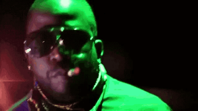 a man wearing sunglasses and a scarf is smoking a cigarette in a dark room .