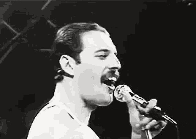 a black and white photo of a man singing into a microphone with his mouth open .