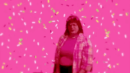 a woman is dancing in front of a pink background with confetti falling from the sky .