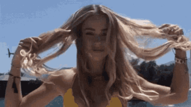 a woman in a yellow bikini is holding her hair in the wind