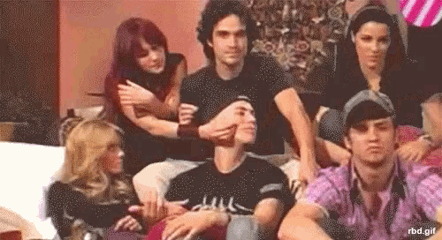 a group of people are sitting on a couch with a man covering his face with his hands .