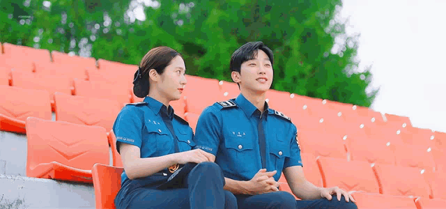 a man and a woman in police uniforms are sitting on a bleacher .