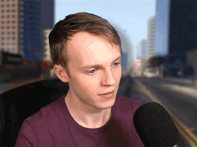 a young man sitting in front of a microphone with a city in the background