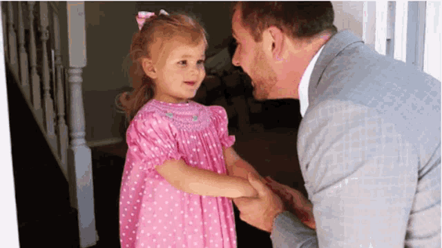 a man in a suit is holding a little girl 's hand in a pink dress .