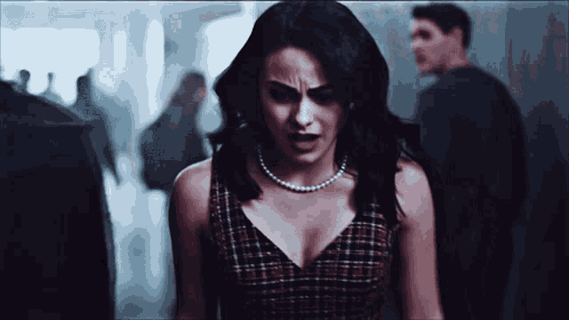 a woman in a plaid dress with a pearl necklace stands in a hallway