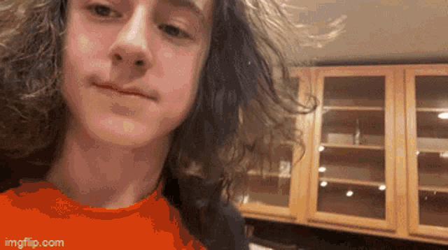 a young man with long curly hair is taking a selfie in a kitchen