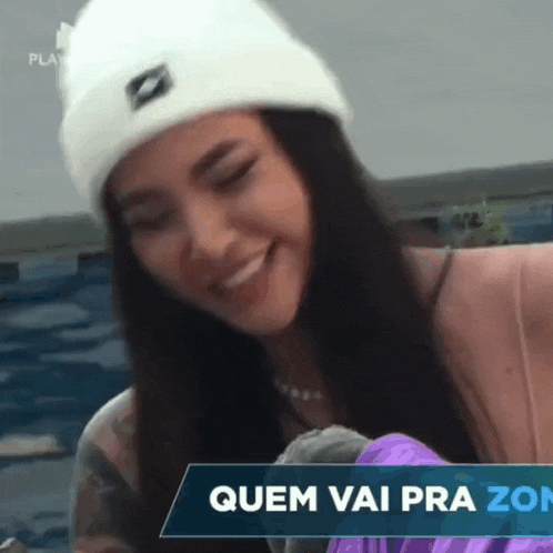 a woman wearing a white hat is smiling in front of a banner that says quem vai pra zon